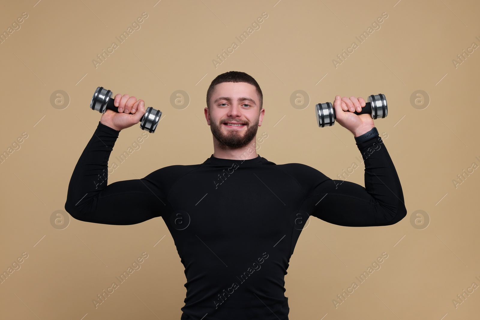 Photo of Handsome sportsman exercising with dumbbells on brown background