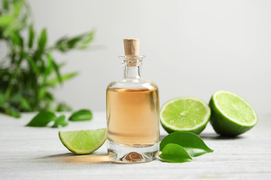 Photo of Lime essential oil and cut citrus fruits on white wooden table