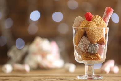 Delicious cookies and candies on wooden table against blurred background, closeup. Space for text