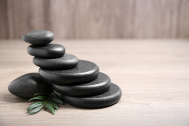 Black spa stones with branch on wooden background. Space for text