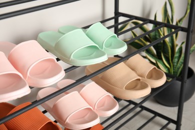 Shoe rack with different pairs of rubber slippers near white wall indoors, closeup