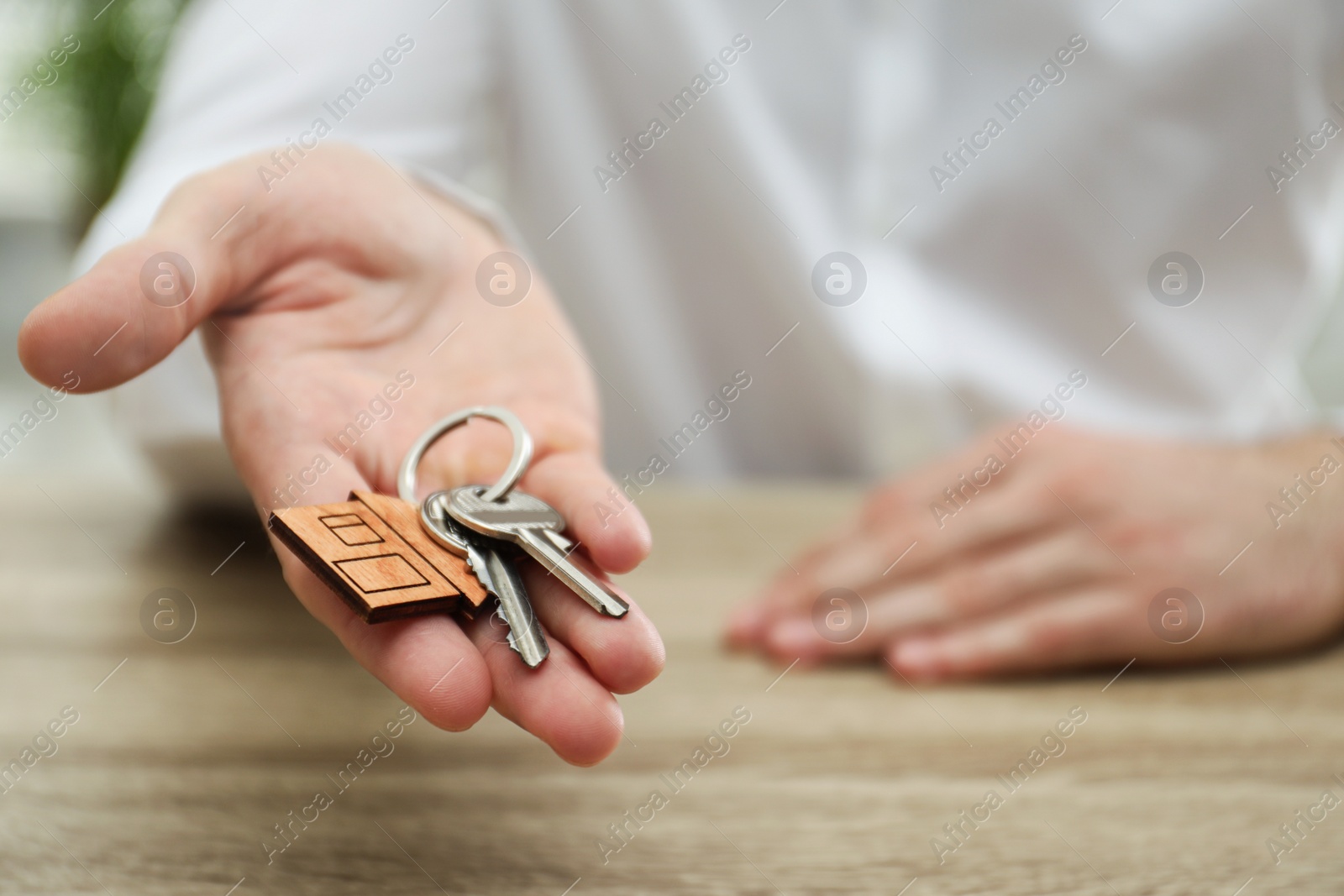 Photo of Real estate agent holding house keys with trinket at wooden table, closeup. Space for text