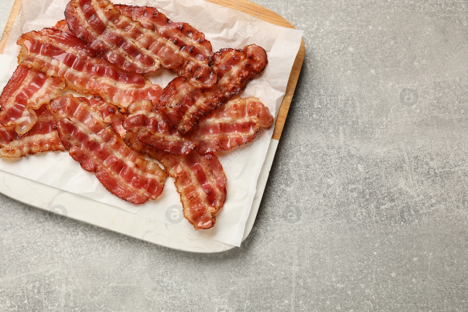 Photo of Board with fried bacon slices on grey textured table, top view. Space for text