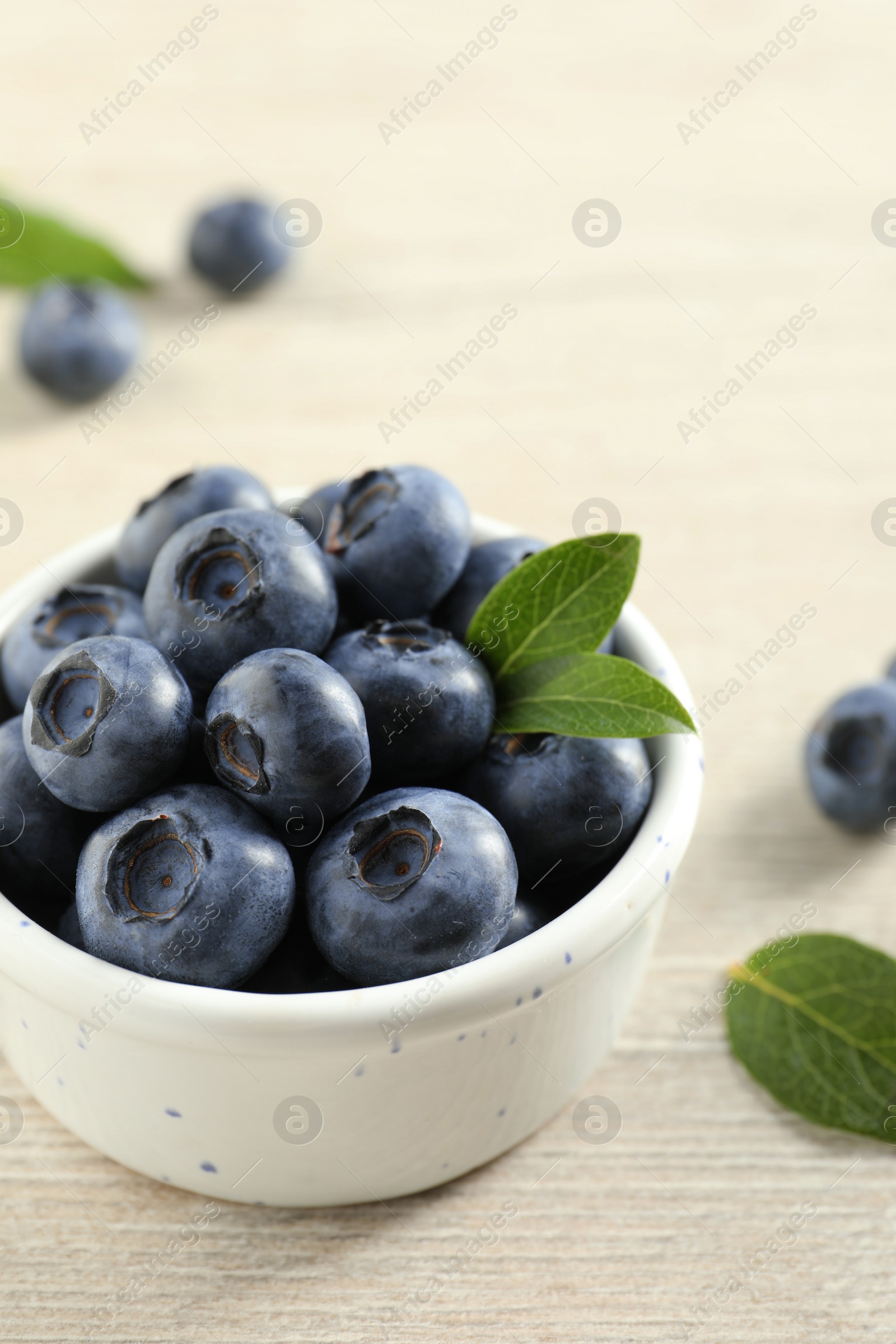 Photo of Bowl of fresh tasty blueberries with leaves on white wooden table, closeup. Space for text