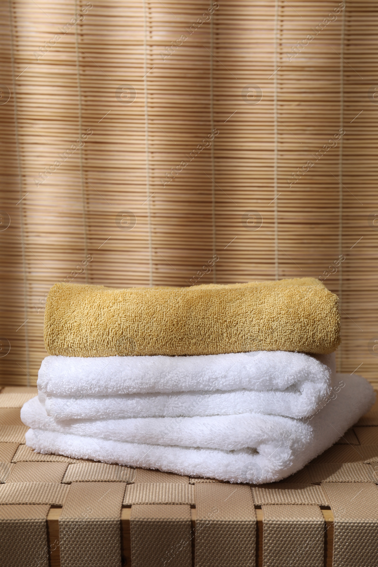 Photo of Stacked soft towels on wicker bench indoors