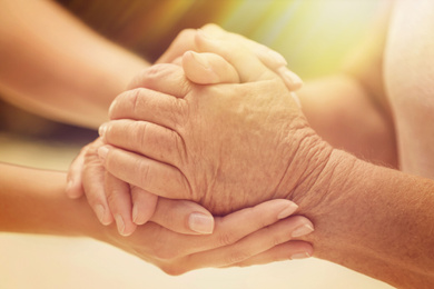 Volunteer and elderly woman holding hands in sunlit room, closeup