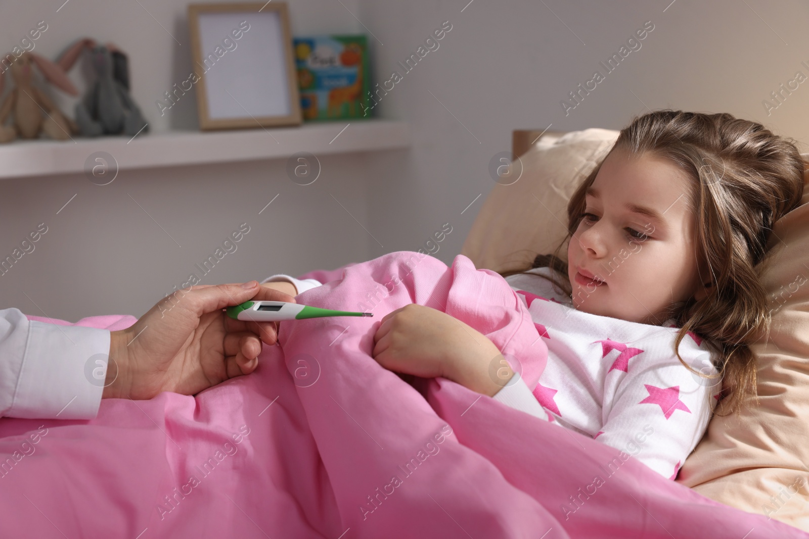 Photo of Doctor with thermometer near little girl in bed indoors