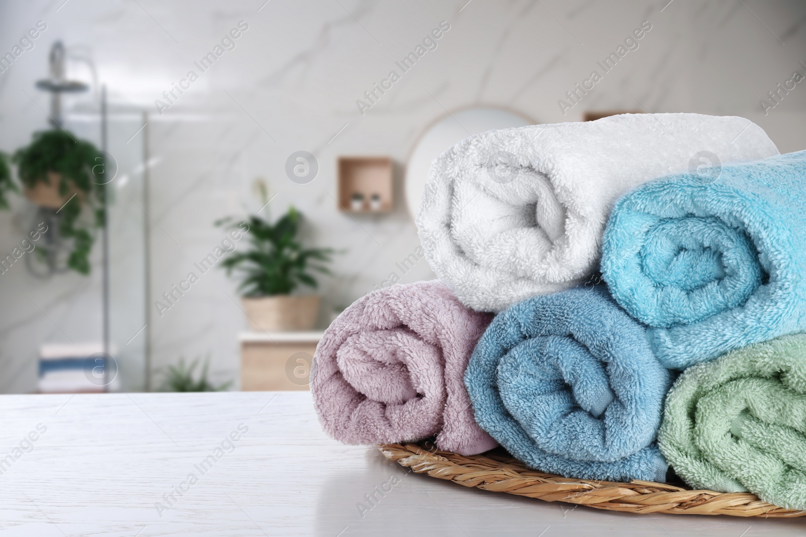 Image of Wicker tray with clean soft towels on white wooden table in bathroom. Space for text