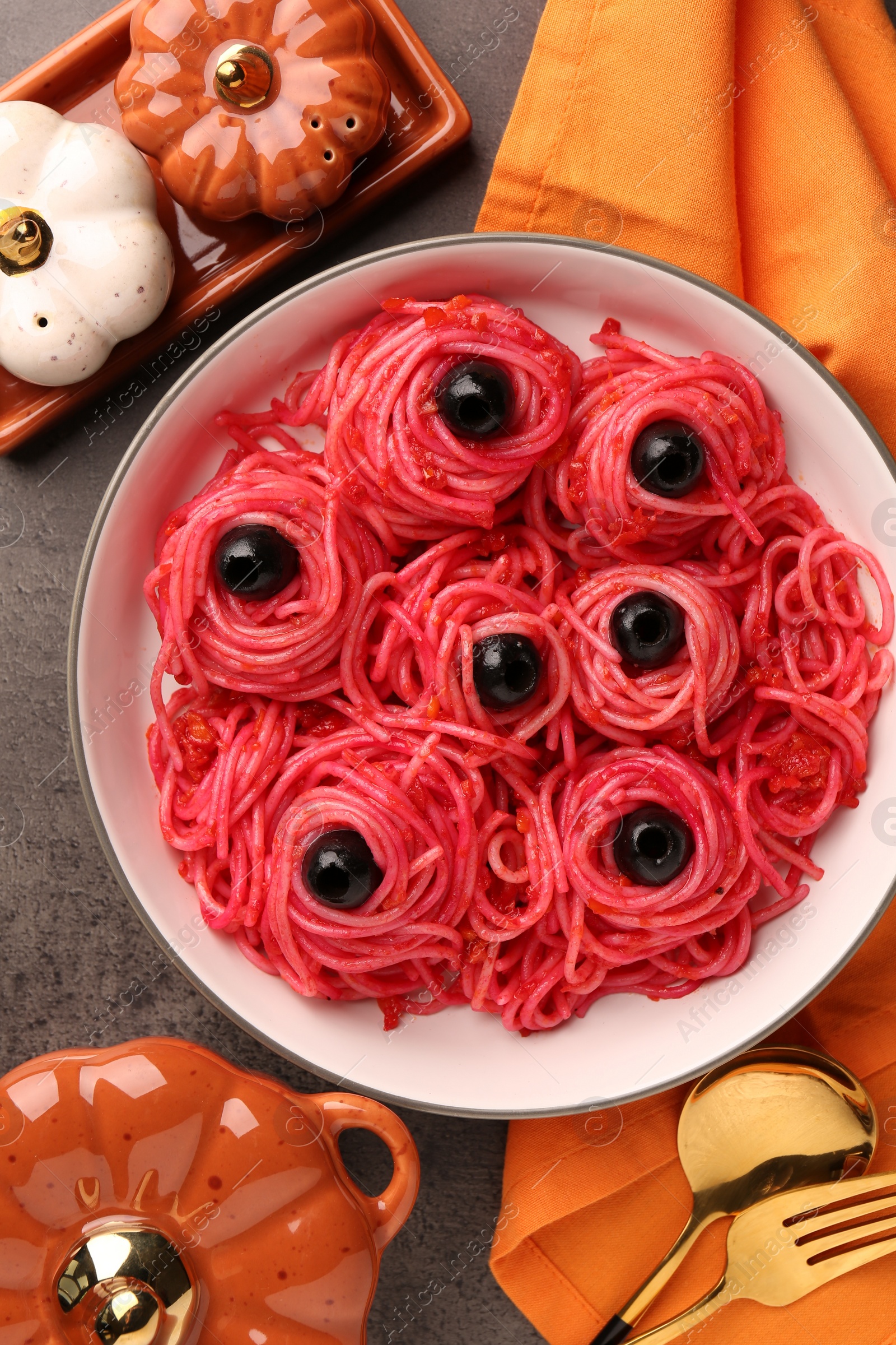 Photo of Red pasta with olives in bowl on grey textured table, flat lay. Halloween food