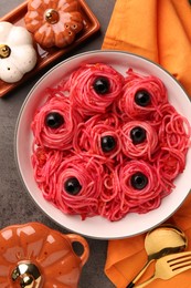 Red pasta with olives in bowl on grey textured table, flat lay. Halloween food