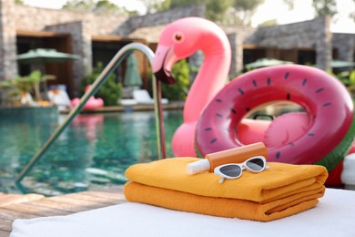 Beach accessories on sun lounger, inflatable ring and float near outdoor swimming pool at luxury resort, space for text