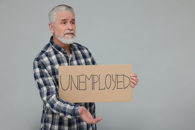 Photo of Confused senior man holding cardboard sign with word Unemployed on light grey background. Space for text