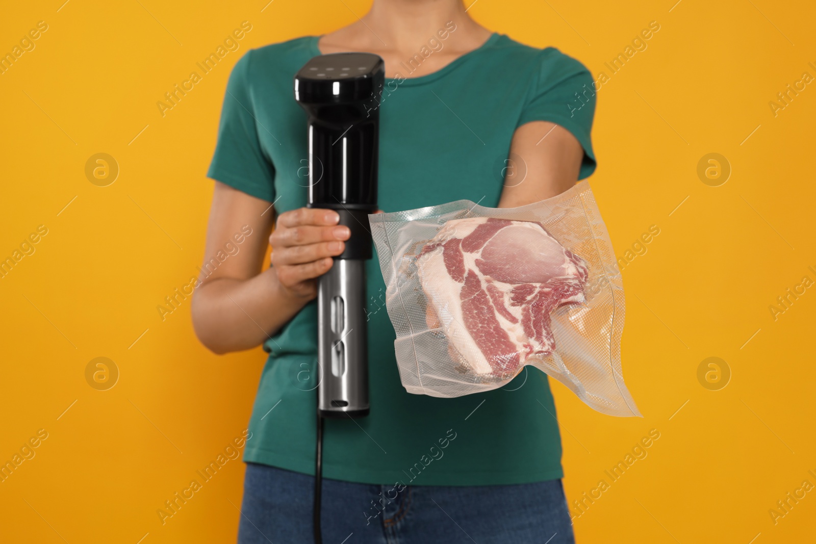 Photo of Woman holding sous vide cooker and meat in vacuum pack on orange background, closeup