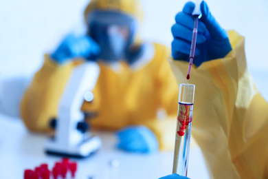 Photo of Scientist in chemical protective suit dripping blood  into test tube at laboratory, closeup. Virus research