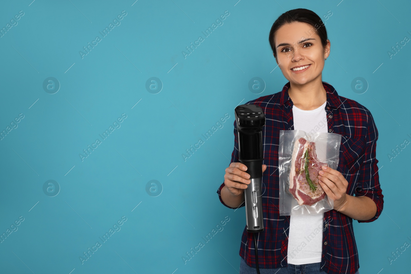 Photo of Beautiful young woman holding sous vide cooker and meat in vacuum pack on light blue background. Space for text