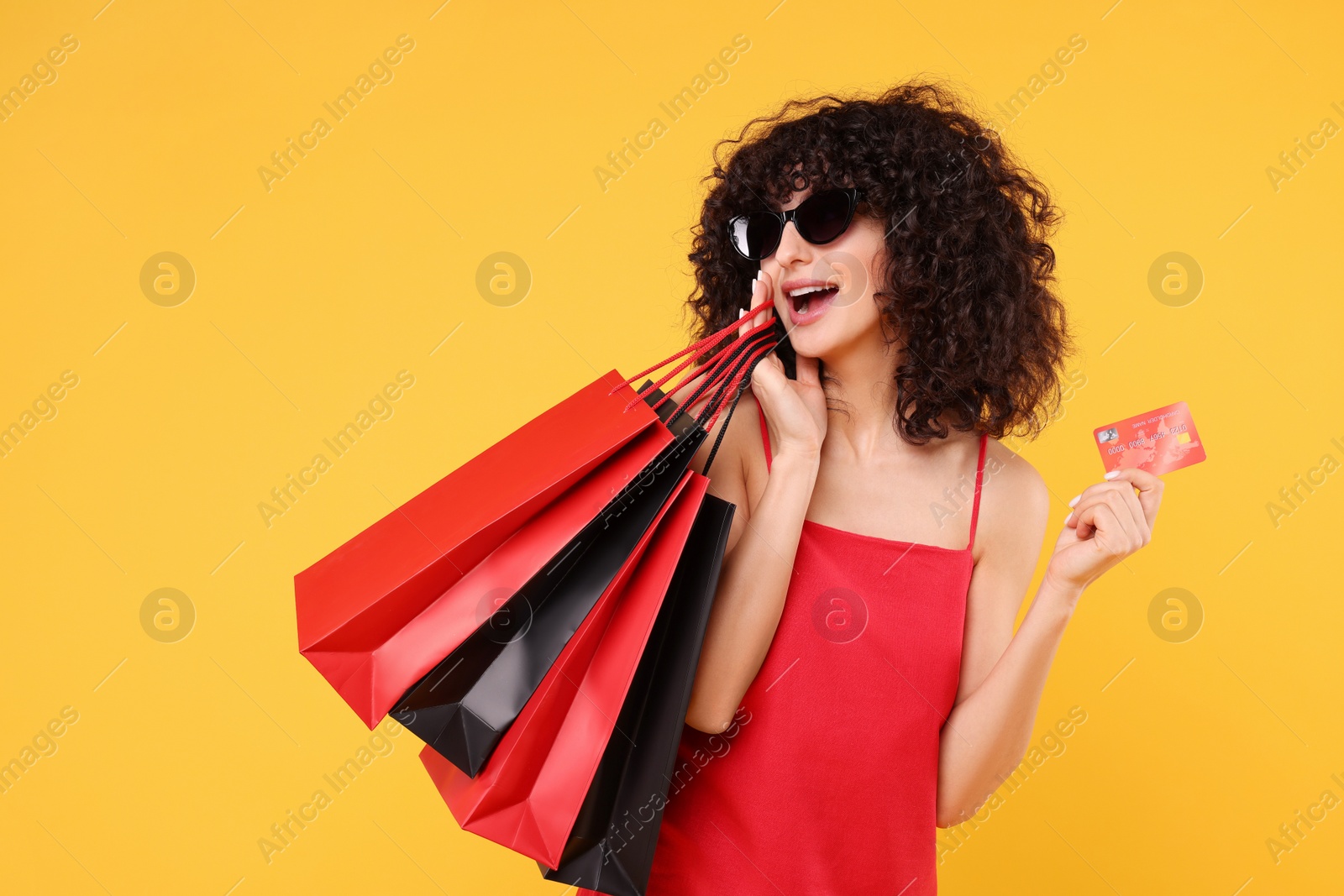 Photo of Happy young woman with shopping bags and credit card on yellow background