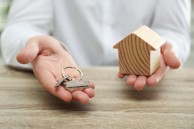 Photo of Real estate agent holding house figure and key at wooden table, closeup