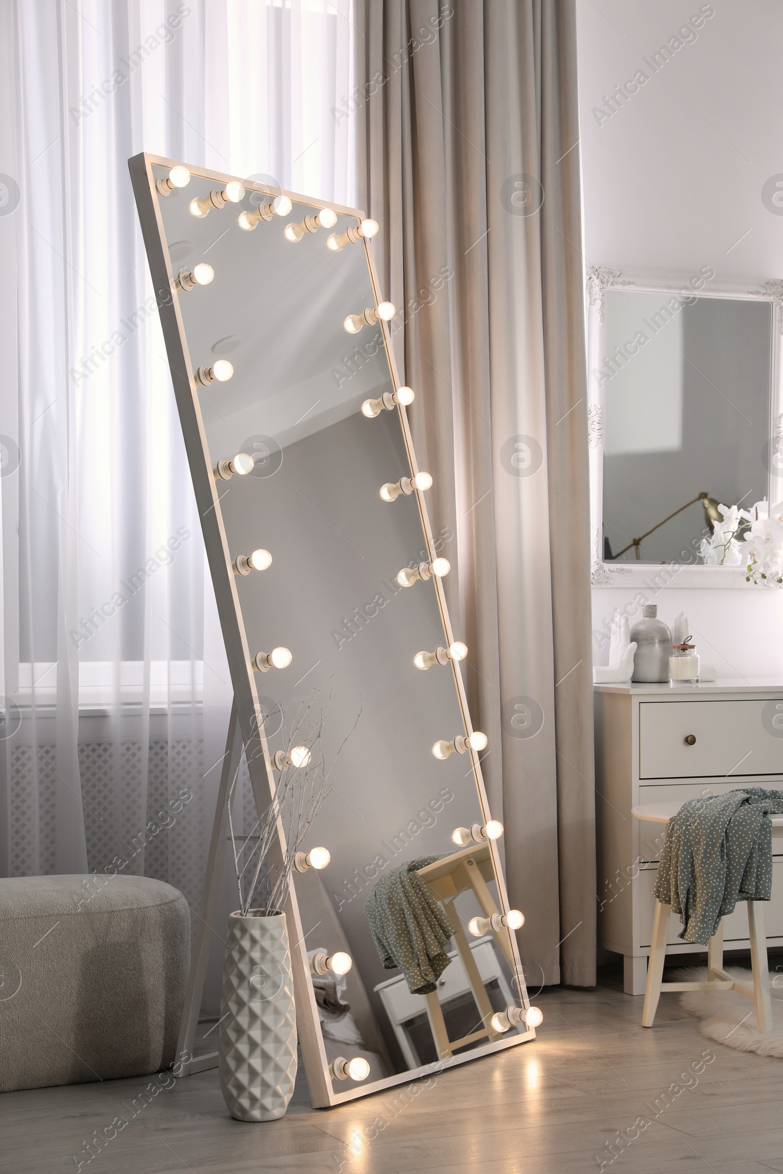 Photo of Large mirror with light bulbs and chest of drawers in stylish room. Interior design