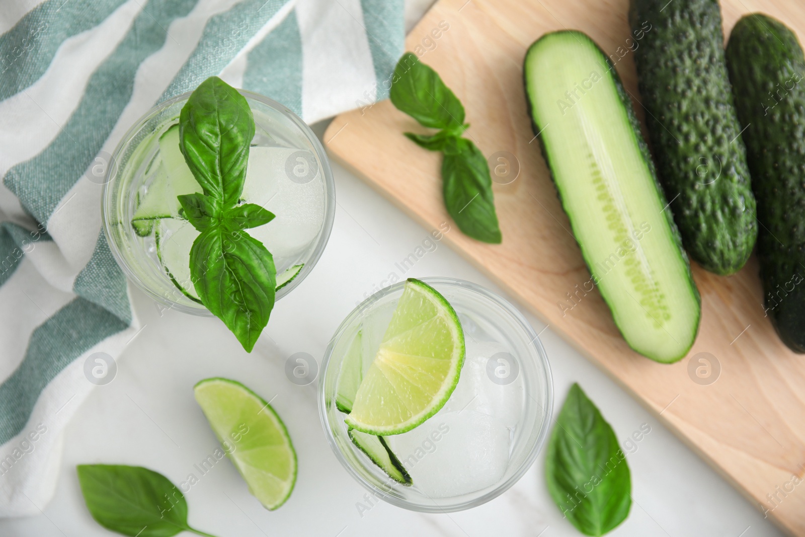 Photo of Tasty fresh cucumber water with sliced lime and basil on white table, flat lay