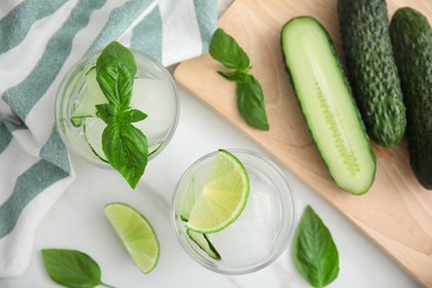 Tasty fresh cucumber water with sliced lime and basil on white table, flat lay