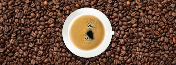 Image of Cup of tasty aromatic coffee on roasted beans, top view. Banner design