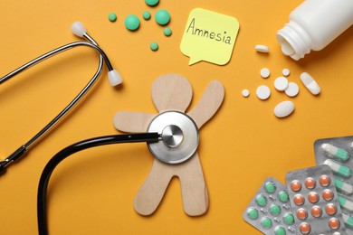 Sticky note with word Amnesia, human figure and drugs on orange background, flat lay