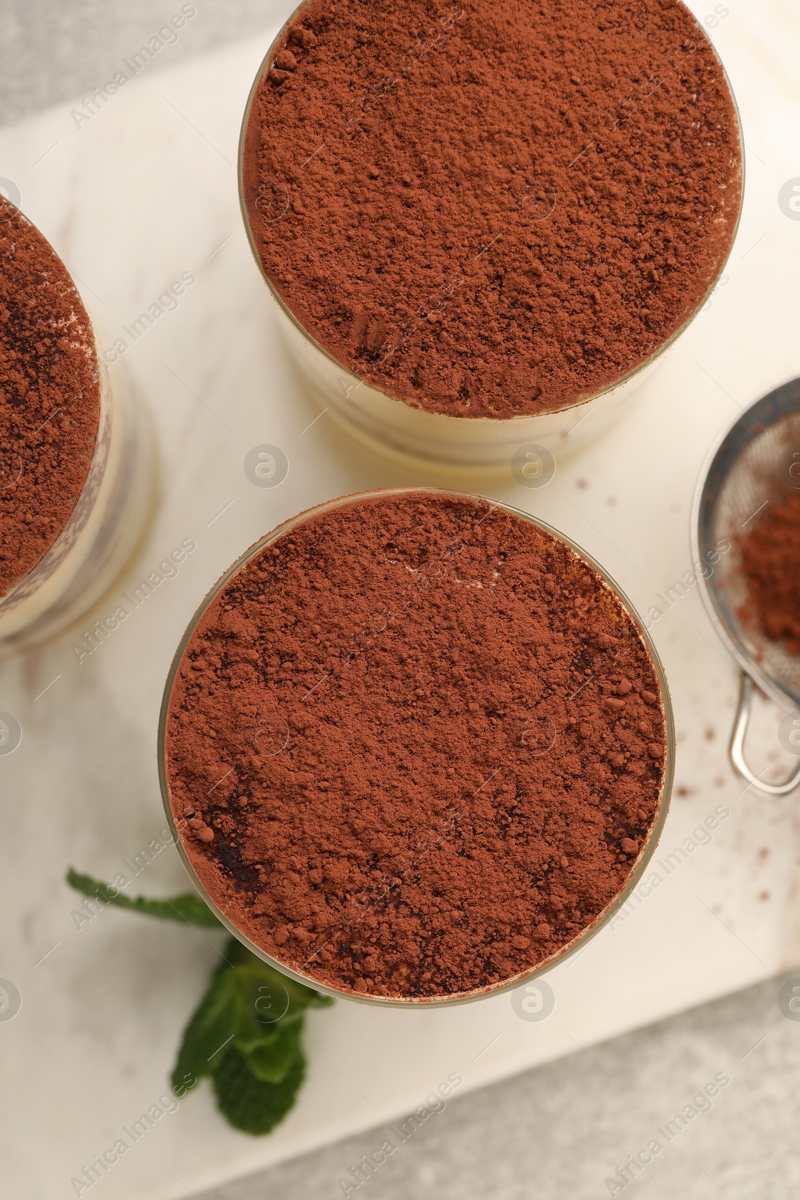 Photo of Delicious tiramisu in glasses and mint on grey textured table, top view