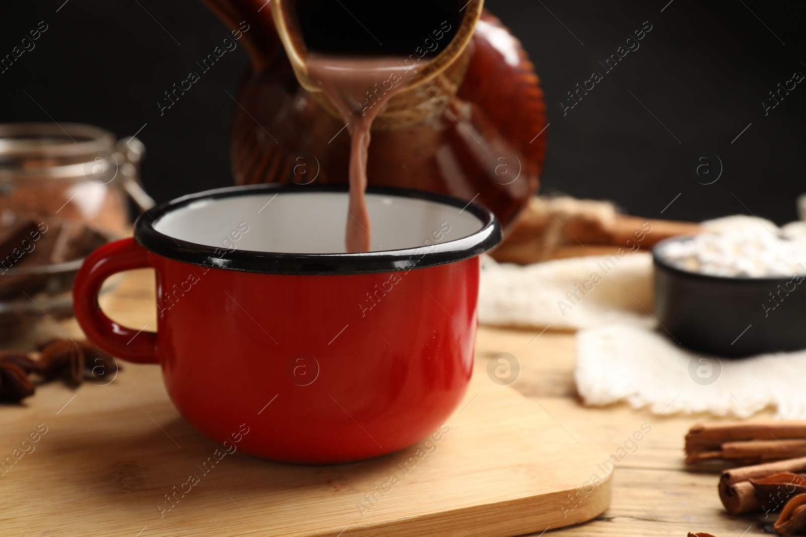 Photo of Pouring tasty hot chocolate into cup at wooden table, closeup