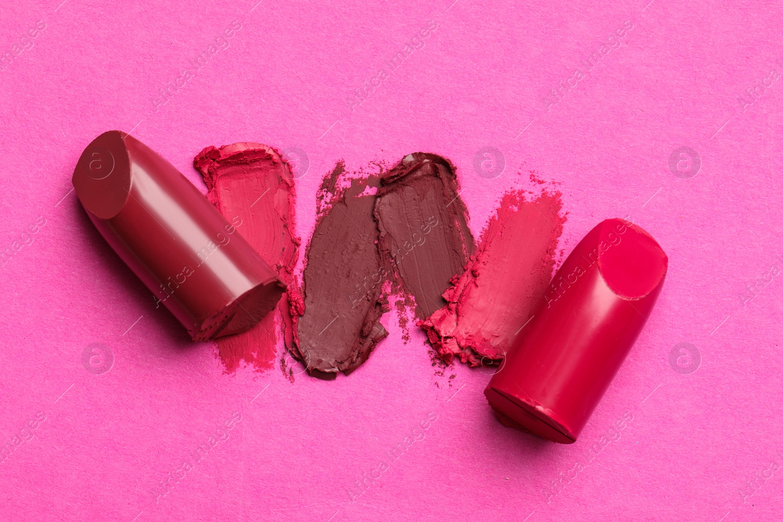 Photo of Different lipsticks and smears on pink background, flat lay