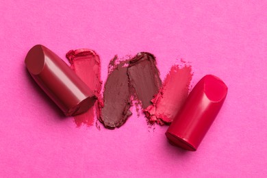 Photo of Different lipsticks and smears on pink background, flat lay