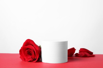Photo of Stylish presentation for product. Round podium, beautiful rose and petals on red table against white background, space for text
