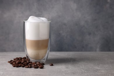 Photo of Aromatic latte macchiato in glass and coffee beans on light grey table. Space for text