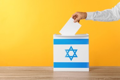 Man putting his vote into ballot box decorated with flag of Israel against yellow background, closeup