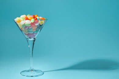 Photo of Beautiful martini glass with colorful candies on light blue background. Space for text