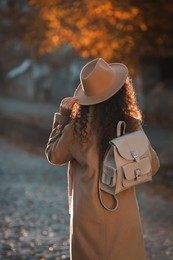 Photo of African-American woman with stylish beige backpack on city street, back view