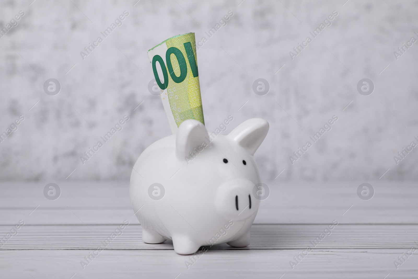 Photo of Ceramic piggy bank with euro banknote on white wooden table. Financial savings