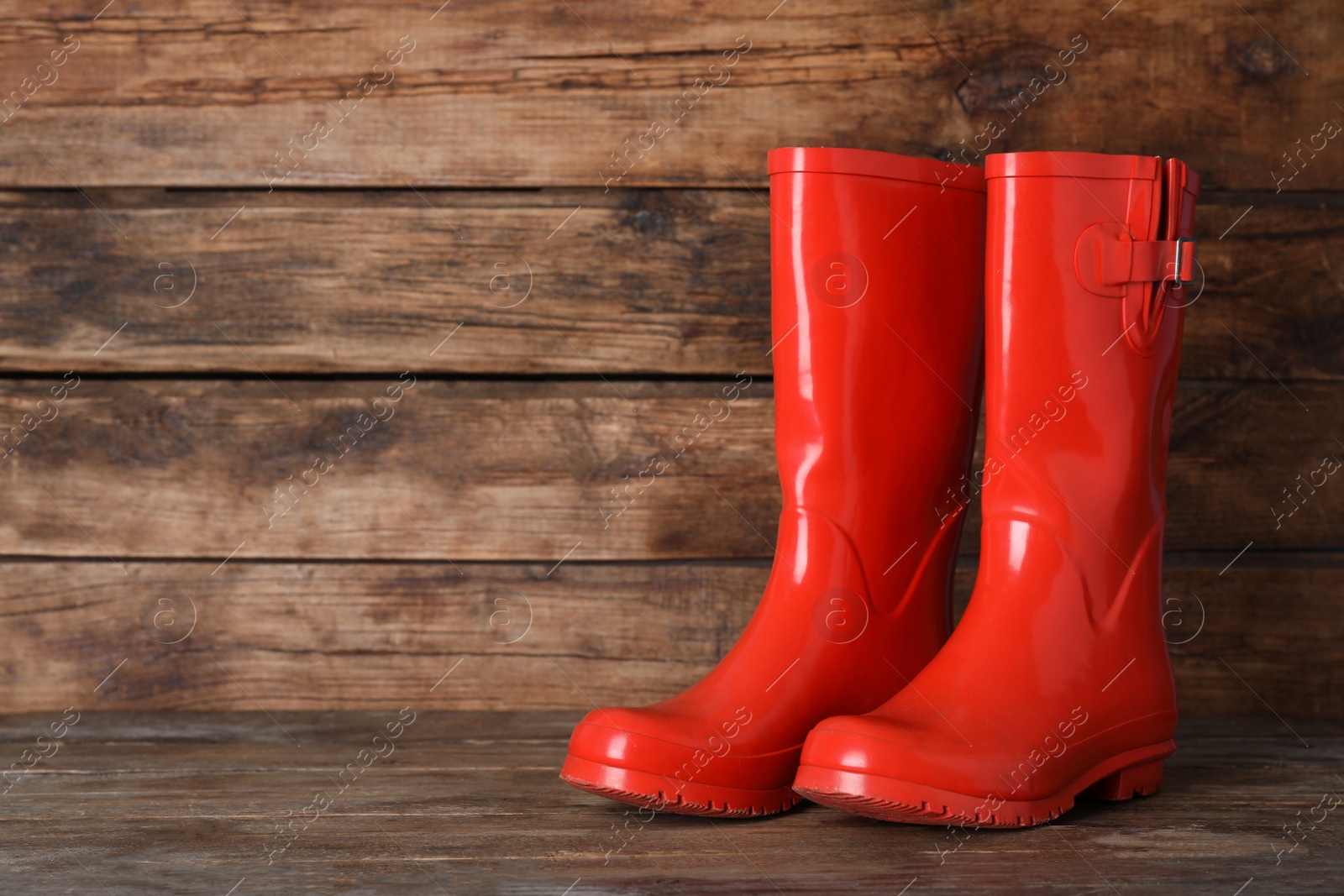 Photo of Pair of red rubber boots on wooden surface. Space for text