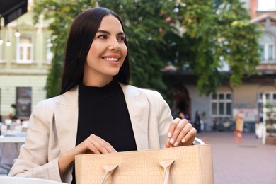Young woman with stylish bag at table in outdoor cafe, space for text