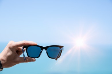 Mature man holding stylish sunglasses against sky, closeup. Space for text