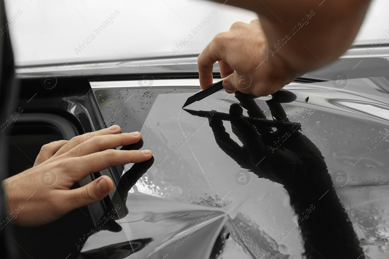 Photo of Worker tinting car window with foil in workshop, closeup