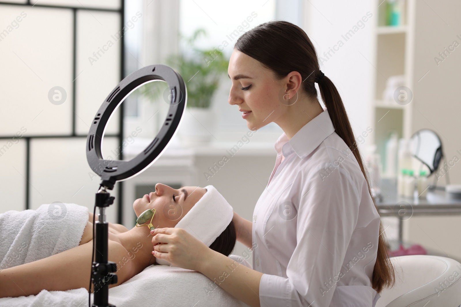 Photo of Cosmetologist making face massage with roller to client in clinic