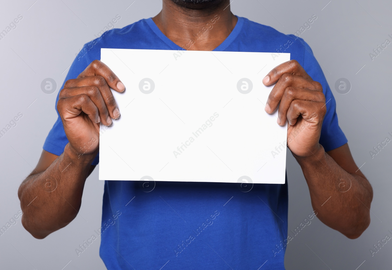 Photo of African American man holding sheet of paper on grey background, closeup. Mockup for design