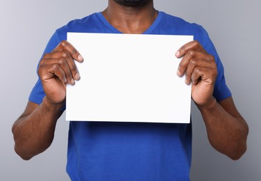 African American man holding sheet of paper on grey background, closeup. Mockup for design