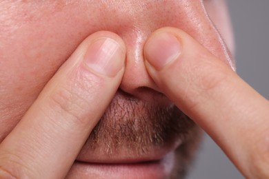 Photo of Man popping pimple on his nose against grey background, closeup