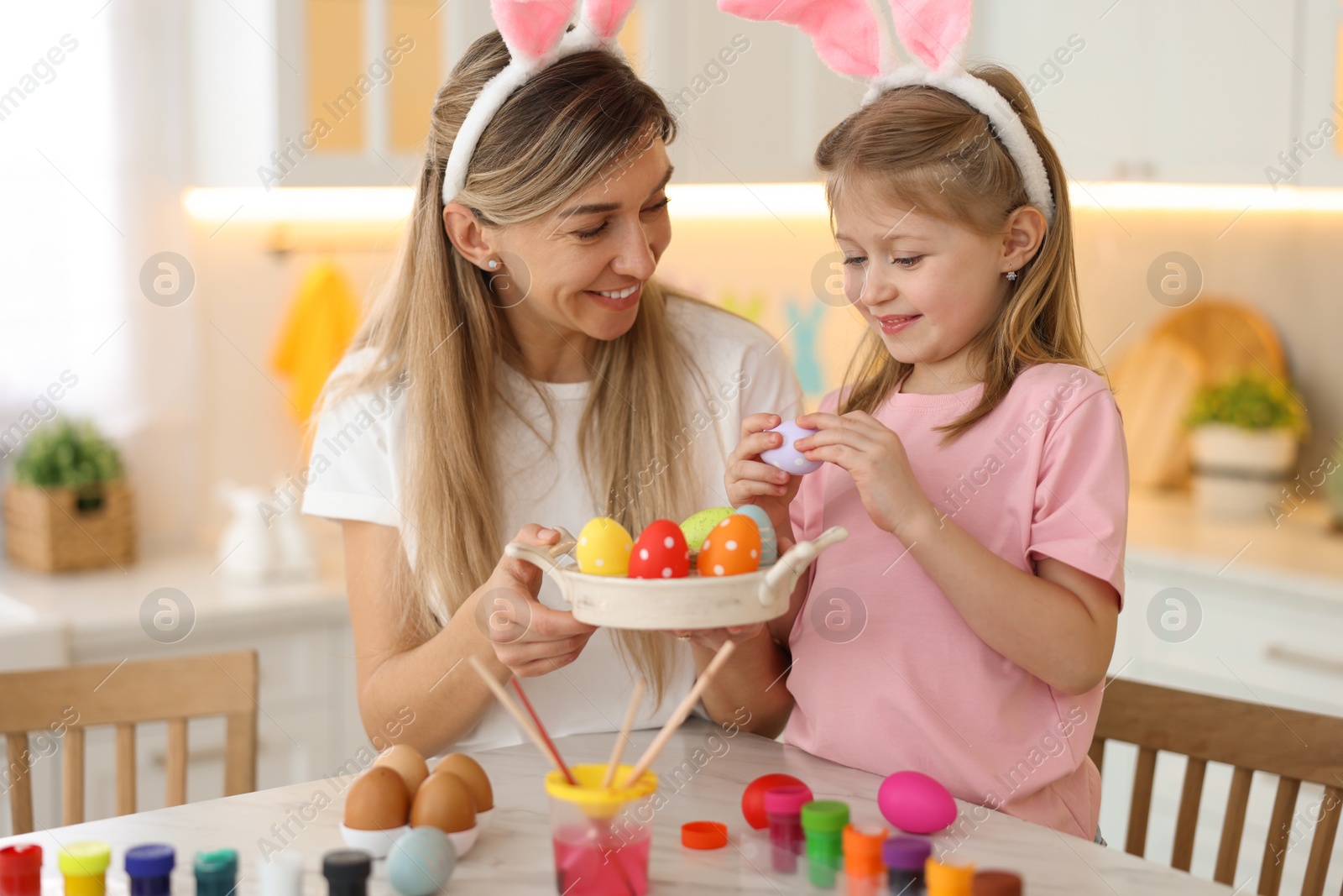 Photo of Easter celebration. Happy mother and her cute daughter with painted eggs at white marble table in kitchen