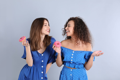 Beautiful young women with donuts on light grey background