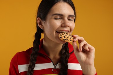 Young woman with chocolate chip cookie on color background, closeup