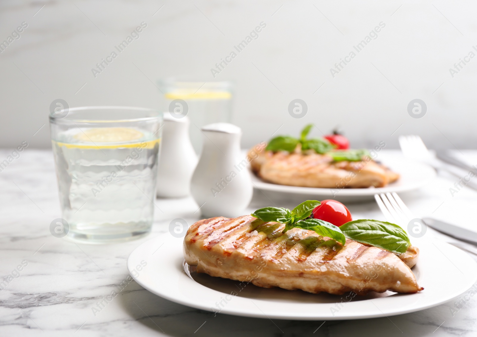 Photo of Tasty grilled chicken fillet with green basil and tomato on white marble table