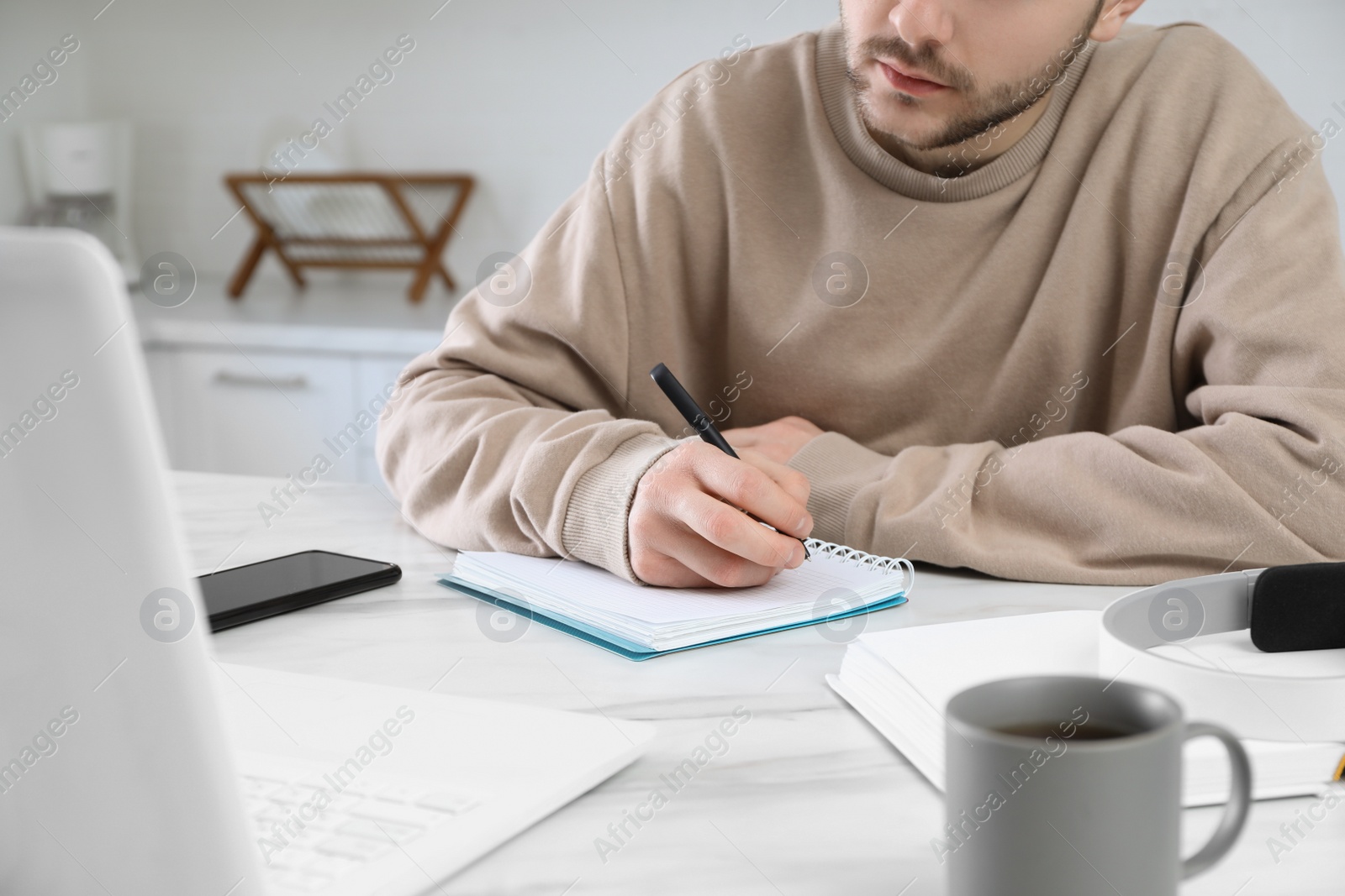 Photo of Young man using modern laptop for studying in kitchen, closeup. Distance learning