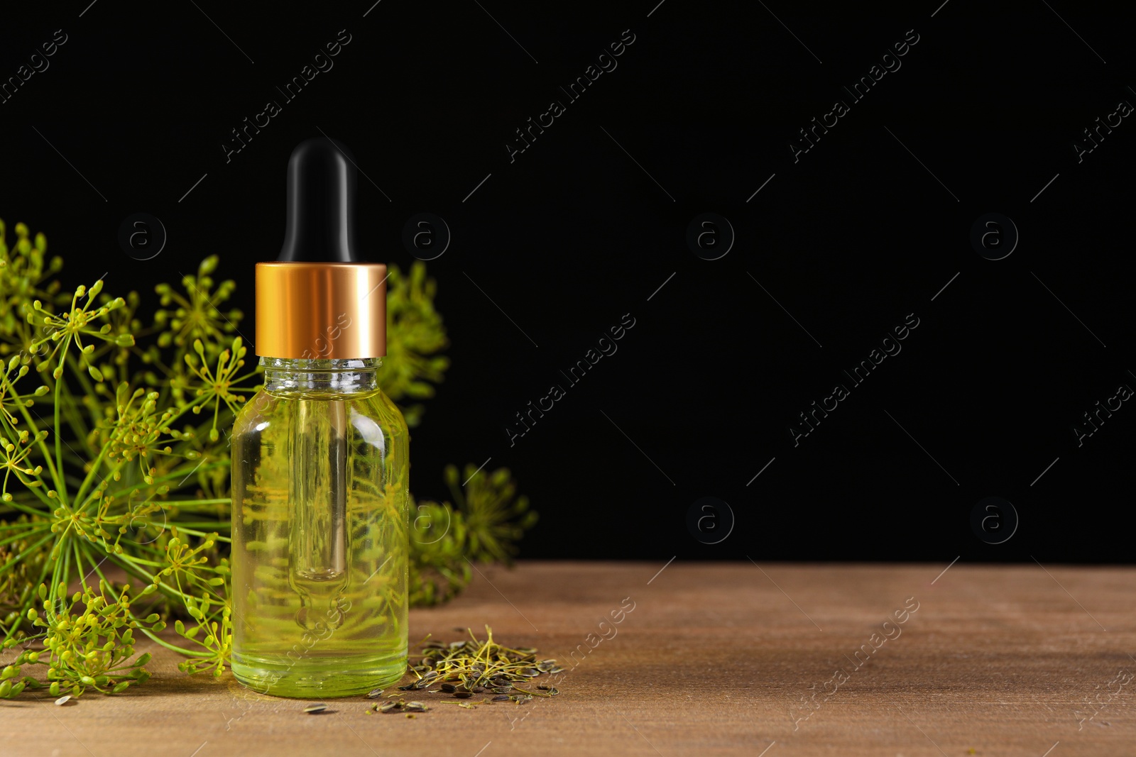 Photo of Bottle of essential oil and fresh dill on wooden table against dark background, closeup. Space for text